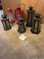 Five lanterns displayed on carpet with a label showing lot number 569: three dark hexagonal lanterns and two red kerosene-style lanterns.