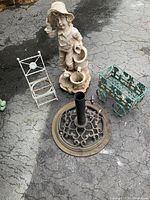 Photo of outdoor decorative items including girl statue, umbrella holder base, wagon and chair plant holders on pavement
