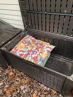 Closed-up angled view of open large outdoor deck storage box showing the wicker-like texture and colorful cushion inside.
