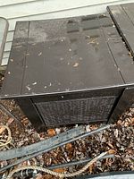 Closed black plastic outdoor deck storage box, showing top and side with dirt and wear.