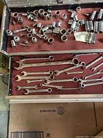 Top and inside view of stainless steel toolbox open showing assortment of combination wrenches and many sockets arranged on red felt lining.