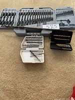 Overview of all drill bit sets and cases on carpeted floor, showing multiple sizes and types of bits.