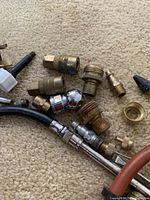 Close-up of various brass fittings and connectors for air compressors laid on carpet.
