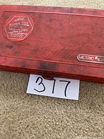 Closed red plastic case labeled Ace Super Hex Taps and Dies Metric #6312, placed on carpeted floor with lot number card.
