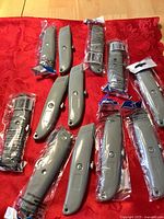 12 gray retractable utility cutters, most sealed in clear plastic packaging on a red cloth background