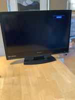 Emerson 32 inch flatscreen TV powered on showing HDMI input on screen, placed on wooden table, black casing with visible Emerson logo.