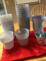Wide view of three stacks of plant pots: white and gray plastic pots with decorative cutout rims, and smaller metal pots with floral design