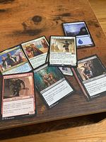 Seven individual Magic: The Gathering cards spread on a wooden surface showing artwork and print details