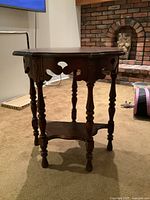 Front angled view of antique carved wood drop leaf side table, showing ornate apron and turned legs.