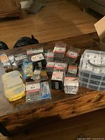 A collection of small boxes and containers with assorted screws, nails, bolts, and anchors placed on a wooden surface.