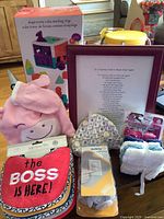 Photo of baby gift set showing shape sorter cube toy box, pink unicorn winter hat, framed poem, gray elephant print hat, Safety 1st plug protectors, bibs, and washcloths.