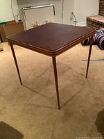 Full view of the folding card table showing brown laminated square top and slim metal legs.