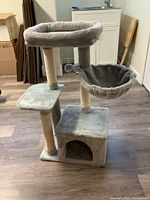 Full view of cat tree showing base, three sisal scratching posts, upper bed, sling basket, and pom-pom ball toy.