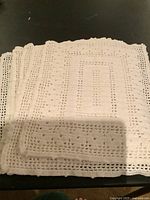 Stack of six white hand crocheted placemats folded on a dark surface showing texture and pattern.