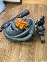 Dyson Stowaway vacuum cleaner showing canister body with orange cyclone separator and attached hose and cleaning head.
