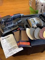 Black & Decker 1/3 sheet sander, instruction manual, and sandpaper packages on a box.