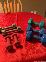 Full view of all seven hand weights on red tablecloth showing color and design variety