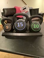 Front view of three kettlebells on stand showing weight numbers 5, 10, 15 pounds in orange, green, and blue respectively.