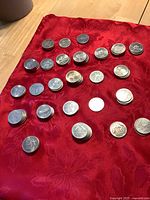 Photo showing multiple stacks and groups of nickel-plated brass coins on a red fabric background, depicting different Olympic sports from the 1980 Winter Olympics.