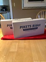 Two unopened boxed PIKETS bidet attachments on table