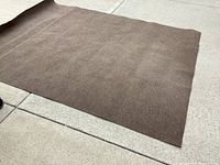Full view of the large brown indoor/outdoor carpet laid on concrete.