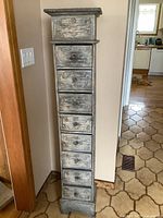 Front view of the tall narrow wooden cabinet with eight carved drawers.