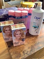 Photo shows 4 multi-packs of pink Always daily liners, 6 cans of Skintimate moisturizing shave gel, 2 boxed packages of Clairol Nice 'n Easy Cream hair color in Light Blonde shade, and one white bottle of Dove Daily Moisture shampoo with pump dispenser on a wooden table.