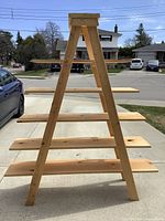 Front view of natural wood A-frame wooden display ladder showing four flat wide shelves spaced evenly. Ladder made from unfinished 2x4 wood boards with visible knots and grain.