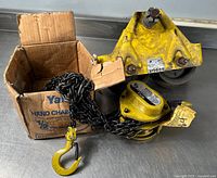 Yale hand chain hoist with chain and yellow hook in original box alongside a yellow metal dolly or trolley component labeled Budgit.
