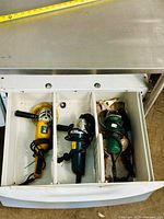Top view of drawer with three angle grinders separated by dividers: yellow Power Fist on left, blue Bosch in middle, green Mastercraft on right.