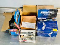 Overview of the four boxed power tools on a table, showing the boxes of Mastercraft angle grinder, Kobalt spray gun, Ryobi grinder, and Power Fist spray gun.