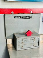 BFGoodrich branded wall-mounted cabinet behind gray three-drawer cabinet topped with red magnetic holder
