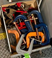 Drawer full of various clamps including blue and orange C-clamps, red quick-release clamps, and silver C-clamps.