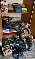 Several corded angle grinders and boxes of discs on floor and shelves of a cabinet