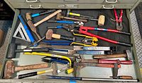 View of drawer contents including mallets, bolt cutters, pry bars, pliers, a square, and a hacksaw all arranged visible on the drawer mat.