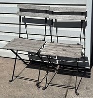 Pair of outdoor patio chairs with cast iron frames and weathered wooden slats for seat and backrest.