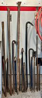 Photo of a lineup of 11 various crowbars and pry bars hanging vertically, showing rust and signs of heavy use.