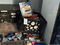 Photo showing black plastic crate filled with staple guns and various boxes of staples alongside a gray metal drawer with more staples.