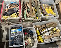 Six plastic bins filled with various straps and bungees including leather, fabric, ratchet straps, and cable tie-downs.