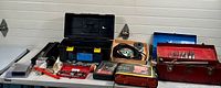 Full view of table with multiple toolboxes, assorted tools, sockets, and small hardware items spread out on a white table.
