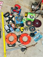 Image showing multiple large tape measures, chalk line reels, orange coaxial reels, and measuring line spools arranged on the floor with a yellow ruler for size reference