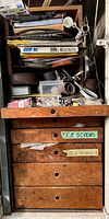 Close-up of one wood cabinet drawer open, showing labeled drawers and various small items and sandpaper inside.