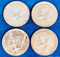 Obverse view of four Kennedy half dollar coins dated 1967 and 1968 laid flat on a blue background showing coin detail and condition.