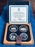 Full view of wooden presentation box open, showing four silver coins and Certificate of Authenticity mounted in lid