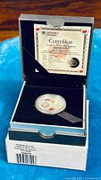 Open display box showing silver coin inside and accompanying certificate.