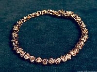 Close-up photo of the sterling silver and cubic zirconia tennis bracelet laid flat against a dark textured background, showing the design and stones.