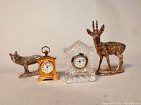 All four items displayed: one Edinburgh Crystal clock, one brass miniature clock, and two pewter animal sculptures (deer and wolf/fox).