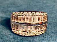 Close-up front view showing the ring's design with baguette-cut CZ stones in two central rows and round CZ stones bordering above and below, on a wide rhodium-plated sterling silver band.