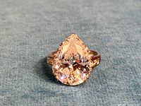 Close-up front view of pear-shaped large clear CZ ring on blue fabric background.