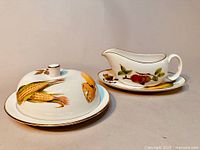 Butter dish with lid and gravy boat with underplate showing fruit designs and gold trim